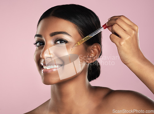 Image of Face, skincare serum and smile of woman in studio isolated on a pink background. Portrait, cosmetics and Indian model with hyaluronic acid, essential oil or vitamin c dropper for healthy dermatology