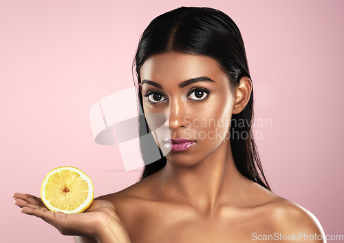 Image of Face, skincare and woman with lemon in studio isolated on pink background. Fruit, serious and portrait of Indian female model with citrus food for healthy skin, vitamin c and detox diet for nutrition