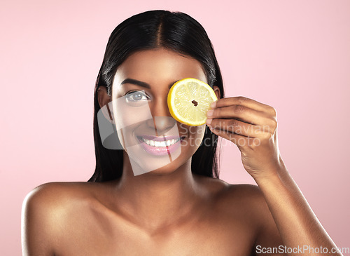 Image of Face, skincare and smile of woman with a lemon slice in studio isolated on a pink background. Fruit, natural cosmetics and portrait of Indian female model with food for detox, nutrition and vitamin c