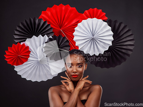 Image of Face, beauty and black woman with origami fans in studio isolated on a dark background. Serious portrait, makeup cosmetics and skincare of female model with traditional Japanese paper art for culture