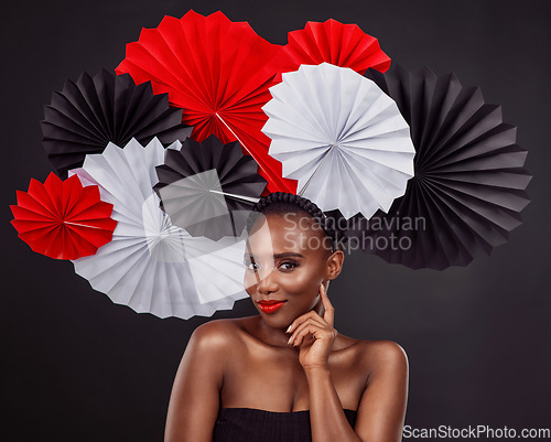 Image of Face, beauty and black woman with origami fans in studio isolated on a dark background. Portrait, makeup cosmetics and skincare of female model with traditional Japanese paper art for fashion hat.