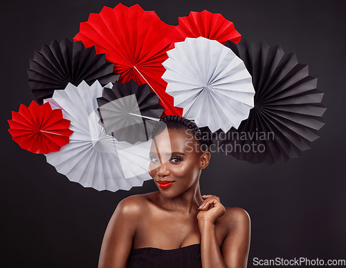 Image of Portrait, skincare and black woman with origami fans in studio isolated on a dark background. Face, makeup cosmetics and beauty of African female model with traditional Japanese paper hat for fashion