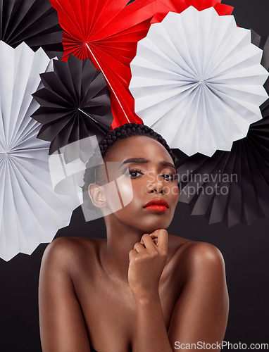 Image of Face, makeup and black woman with origami fans in studio isolated on a dark background. Portrait, beauty cosmetics and skincare of serious female model with traditional Japanese paper hat for art.