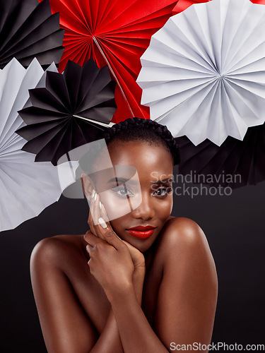 Image of Portrait, beauty and black woman with origami fans in studio isolated on a dark background. Natural face, makeup cosmetics and skincare of female model with traditional Japanese paper art for culture