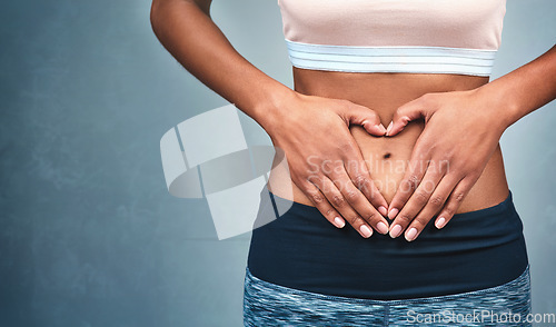 Image of Heart, fitness and hands of a woman on a stomach isolated on a dark background in studio. Wellness, gut health and a girl with shape for love of body, weight loss and abdomen digestion on backdrop