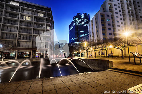 Image of Night, cityscape and urban buildings at dark with lights in Cape Town outdoor with no people. Street, lighting and city infrastructure with fountain and skyline at evening outdoors with a road