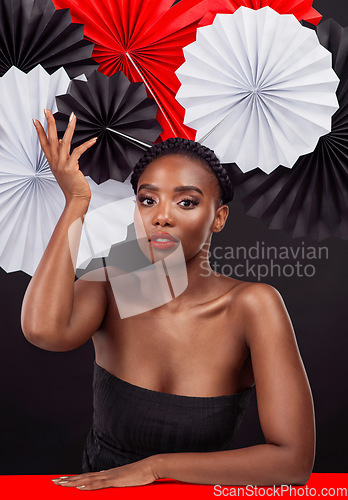 Image of Portrait, beauty and black woman with origami fans in studio isolated on a dark background. Natural face, makeup cosmetics and skincare of female model with traditional Japanese paper art for culture