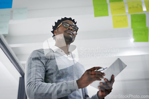 Image of Business tablet, glass wall and black man brainstorming, strategy or research ideas in office. Sticky notes, planning and African male professional with technology for working, schedule and low angle