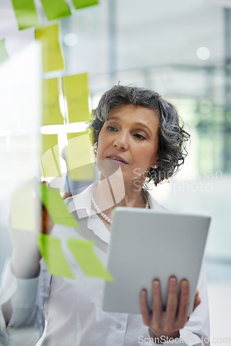 Image of Glass wall, tablet and business woman writing, planning and strategy in office workplace. Sticky notes, brainstorming and senior female professional with technology for working, schedule and info.