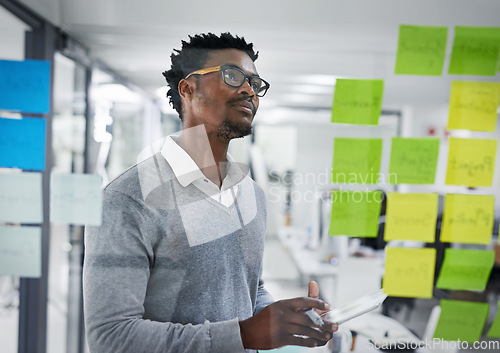 Image of Business tablet, glass wall and black man planning, strategy or research in office workplace. Sticky notes, brainstorming and African male professional with technology for working, schedule and ideas