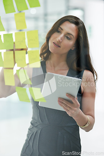 Image of Tablet, glass wall and business woman writing, planning and strategy in office workplace. Sticky notes, brainstorming and female professional with technology for working on ideas, schedule and info.