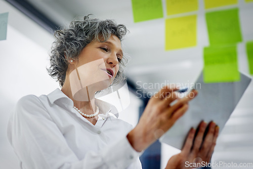 Image of Glass wall, tablet and business woman planning, strategy and research in workplace. Sticky notes, brainstorming and senior female professional with technology for working, schedule and low angle.