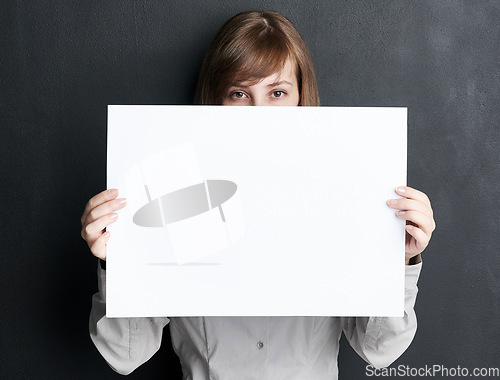 Image of Portrait, poster and mockup with a woman in studio on a dark background for information or announcement. Branding, advertising or marketing with a young female brand ambassador holding a blank sign
