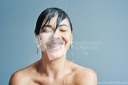 Image of Beauty, water splash and face of woman shower on blue background for wellness, cleaning and grooming. Skincare, bathroom and happy female person for washing hair, body care and cleansing in studio