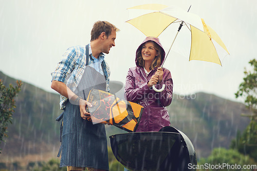 Image of Man, woman and barbecue in rain with umbrella, charcoal or surprise on vacation with love in garden. Couple, outdoor and grill in storm, backyard or cooking in winter with helping hand, wind or smile