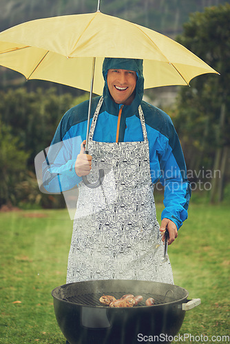 Image of Happy man, portrait and umbrella in rain for barbecue meal, supper or dinner on the fire grill. Male person smiling for insurance, cover or protection while cooking under raining or stormy weather