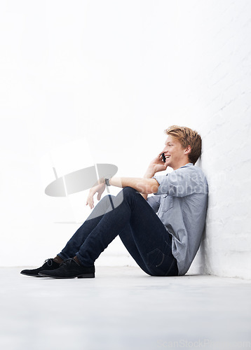 Image of Man, phone call and floor with space by wall with smile, communication and talk at startup. Young businessman, entrepreneur and sitting for conversation on smartphone with mockup at small business