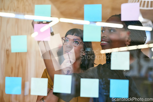 Image of Business people, thinking and planning with notes in a creative office for designer project. Women team together for collaboration, teamwork and ideas on a glass wall with color paper and diversity