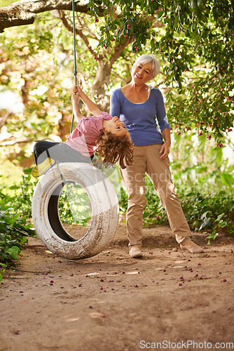 Image of Elderly woman, garden and grandchild playing with grandma or holidays and having fun on a tyre swing in summer. Excited, grandkid and outdoors on jungle gym together or on sunny weekend at a park