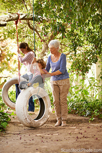 Image of Senior woman, garden and grandma pushing her grandchildren on a tyre swing or holidays and having fun in summer. Excited, grandkids and elderly woman outdoors on jungle gym or on sunny day at a park