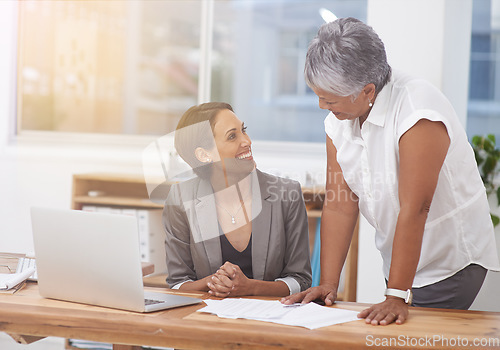 Image of Business women, desk and talking in office for planning, training or advice. Manager or coach and employee together for discussion, collaboration or teamwork with a laptop and paperwork at workplace