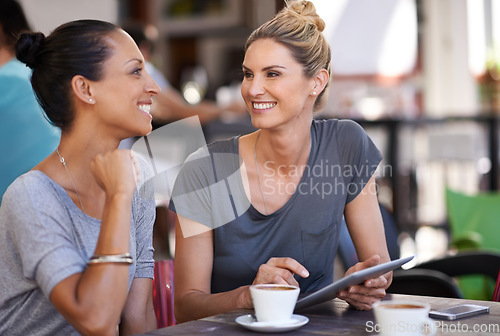 Image of Tablet, discussion and women drinking coffee at a cafeteria together talking and scrolling on social media. Happy, smile and friends speaking, laughing and enjoying a capuccino at restaurant in city.
