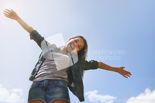 Image of Portrait, blue sky and arms with a woman outdoor in nature for fun, freedom or adventure in summer from below. Smile, health and wellness with a happy young female person outside to celebrate life