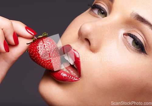 Image of Beauty, portrait and model with a strawberry in studio with red nails and lipstick cosmetics. Health, wellness and closeup of woman with makeup eating fruit for nutrition isolated by gray background.