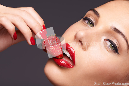 Image of Makeup, portrait and woman with a strawberry in a studio with red nails and lipstick cosmetics. Health, wellness and closeup of a female model eating fruit for nutrition isolated by a gray background