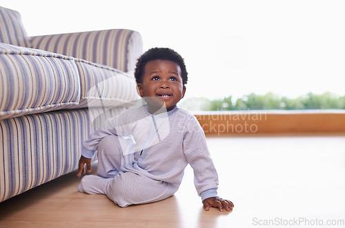 Image of Black baby boy sitting on floor in living room, childhood development with growing happy kid at family home. African male toddler, cute child relax on wood floor with growth and learning mobility