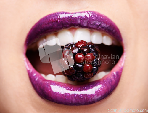 Image of Closeup of woman lips with purple lipstick, makeup and beauty with shine and vibrant aesthetic, creativity and glow. Fruit between female model teeth, cosmetic product for mouth and cosmetology