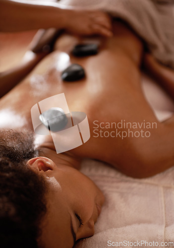 Image of Hands, hot stone massage and woman in spa with luxury service for muscle, body and relax with peace in resort. Masseuse, hospitality and physical therapy on bed for wellness, zen and natural healing