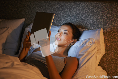 Image of Woman, night and bed for reading on tablet, website or social media app to relax in home, hotel or apartment. Girl, mobile touchscreen and happy with ebook, movie or video on internet in bedroom