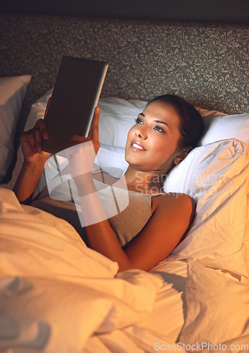 Image of Woman, night and bedroom for reading on tablet, website or social media app to relax in home, hotel or apartment. Girl, mobile touchscreen and happy with ebook, movies or video on internet in bedroom