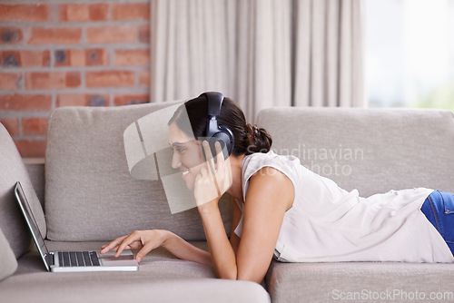 Image of Woman, laptop and lying on couch with headphones for streaming, music and search for web video in home. Girl, smile and scrolling for movie, podcast or meme on internet to relax on sofa with computer