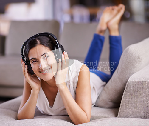 Image of Happy woman, headphones and listening to music with smile on sofa for free time, comfort or relaxing at home. Female lying on living room couch with headset for audio sound track or relax on holiday