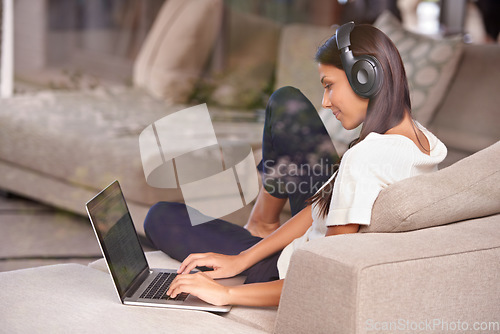 Image of Headphones, typing and woman with laptop on home sofa listening to music, audio or streaming movies. Happy female student relax on couch to listen to podcast or research to learn language on internet