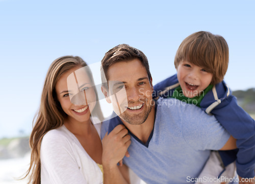 Image of Beach, family and summer portrait outdoor for travel, adventure or holiday and piggy back fun. A man, woman and child or son playing together on vacation at sea with a blue sky, parents and happiness