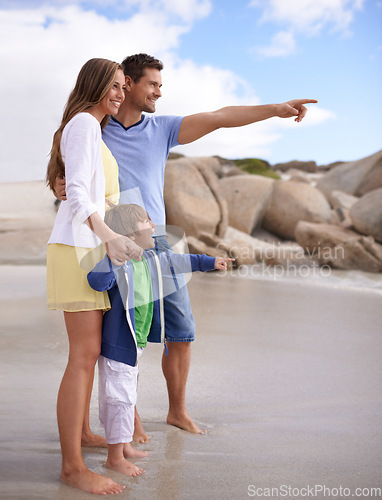 Image of Family, child and pointing outdoor at beach for travel, adventure or holiday in summer with a smile. A man, woman and kid or son together on vacation at sea for blue sky, learning and happiness