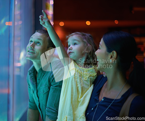 Image of Family, aquarium and child pointing at fish for learning, curiosity or knowledge, bonding or care. Mother, fishtank and happy kid with father watching marine animals swim underwater in oceanarium.