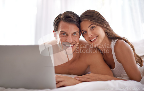 Image of Laptop, love and portrait of a couple in bed together while watching a online movie or video at their home. Happiness, smile and woman browsing the internet on computer with her husband in bedroom.