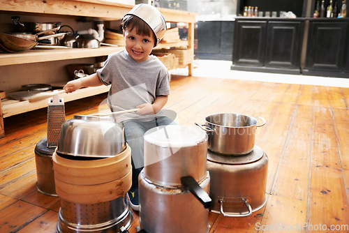 Image of Portrait, boy child and playing drum on a pot on a floor, happy and enjoying playful music. Face, creative and kid with pan for musical instrument, fun and carefree in a kitchen on the weekend