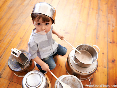 Image of Portrait, boy child playing drums on pots on a floor, curious and enjoying music. Face, top view and kid with pans for musical entertainment, silly and carefree in kitchen in his home on the weekend