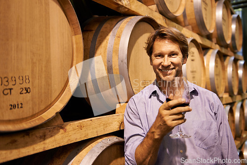 Image of Portrait, smile and wine tasting with a man in the cellar of a distillery on a farm for the production of alcohol. Glass, industry and barrel with a happy male farmer drinking for quality control