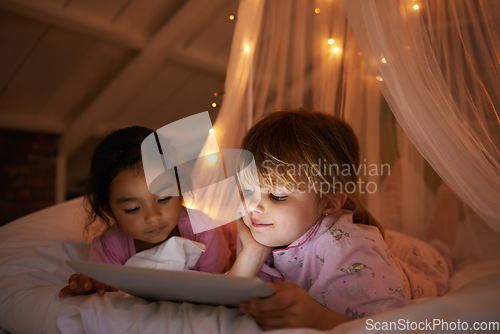 Image of Girls, bedroom and tablet for a movie, night and relax with pajamas, chilling and games at home. Female children, young people and kids with technology, bed or bonding with fun, playful and happiness