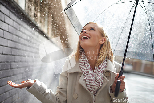 Image of Smile, excited woman and rain in the city with umbrella, freedom and happiness on holiday. Winter weather, raining or urban street with a young female person on a sidewalk and travel vacation outdoor