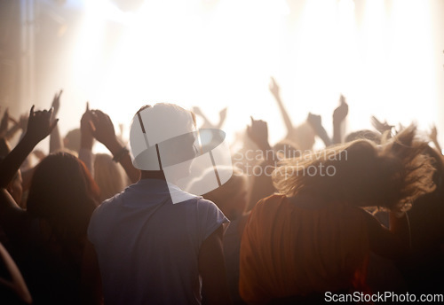 Image of Fans, people dancing at music festival from back, stage light and energy at live concert event. Dance, fun and excited crowd in arena at rock band performance or audience at show or techno rave party