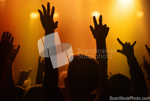 Image of Orange lights, hands of people at concert or music festival dancing with energy in silhouette at live event. Dance, fun and group of excited fans in arena at rock band performance or crowd at party.