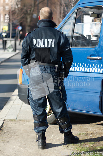 Image of Police man, van and security in the city of Denmark for street safety, service or law enforcement patrol. Back of male officer standing ready to fight crime for justice or riot control in urban town