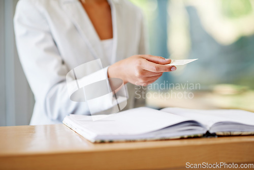 Image of Woman, hands and business card at reception for information, gift or payment on desk at resort. Hand of female receptionist giving voucher at counter for discount, paying or check in at appointment